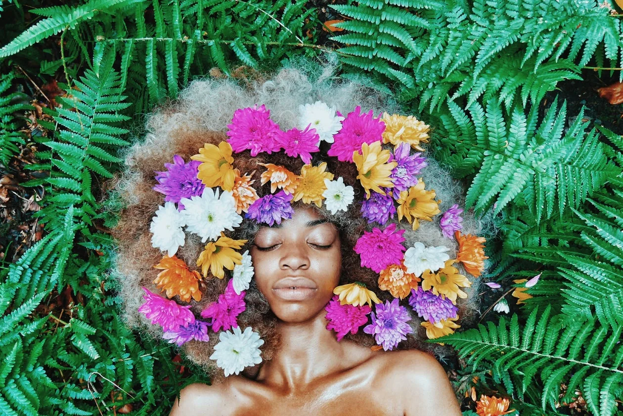 Frau mit voluminösem Naturafro, in dem bunte Blüten stecken