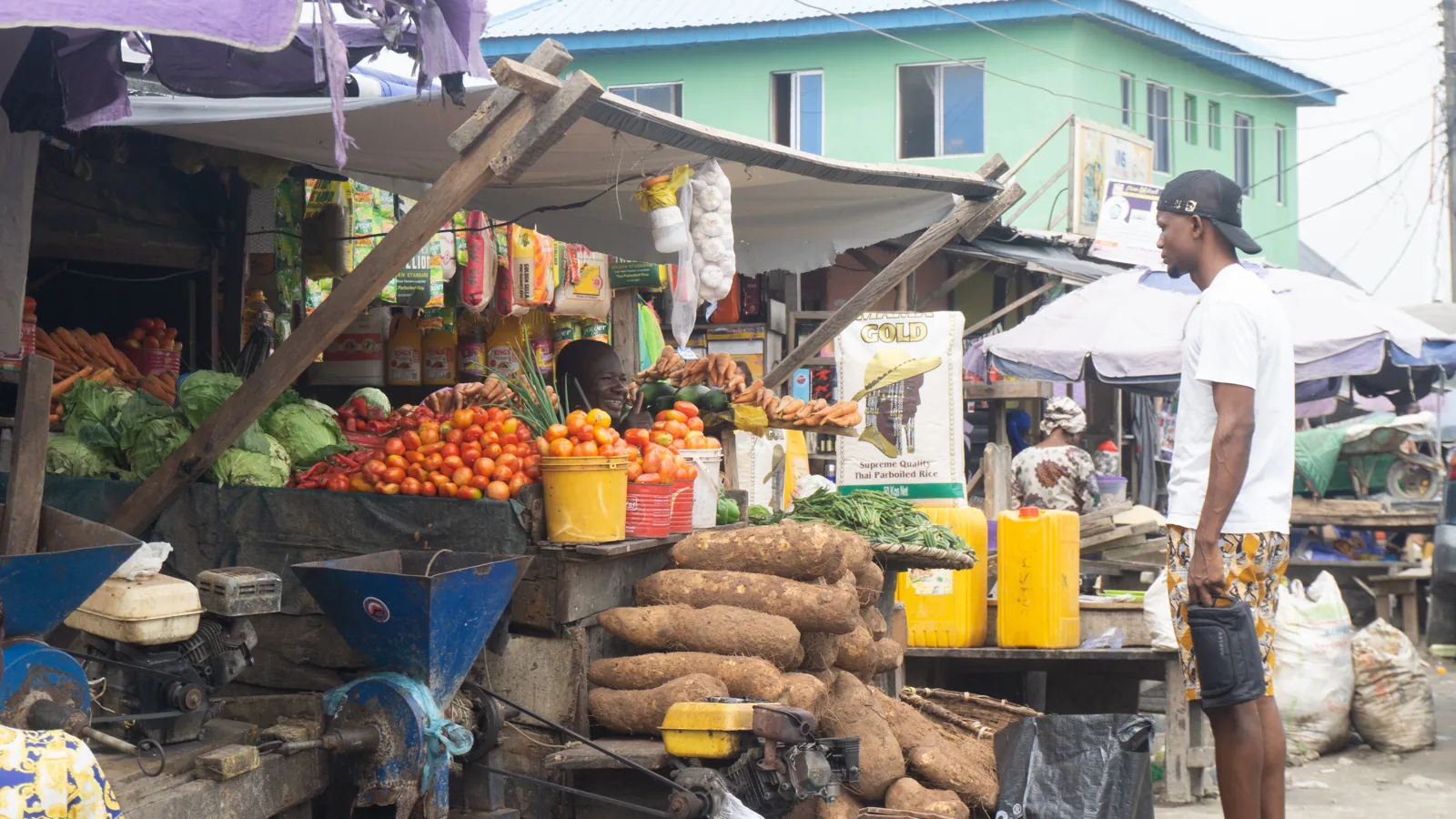 Lachender Verkäufer hinter Tomaten, Kohl und Yams an einem Marktstand in Lagos
